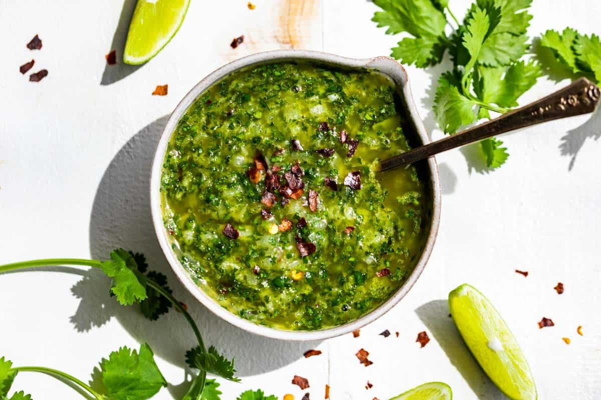 Cilantro Chimichurri in a pottery bowl surrounded by lime wedges and cilantro sprigs.