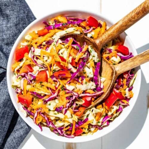 A large white serving bowl filled with Cilantro Lime Slaw and wooden serving spoons.