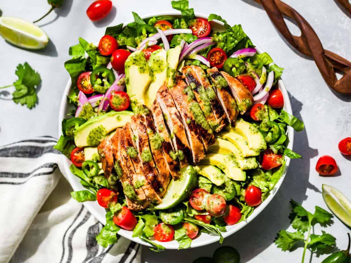 Guacamole Salad topped with sliced chipotle chicken surrounded by cilantro and cherry tomatoes.