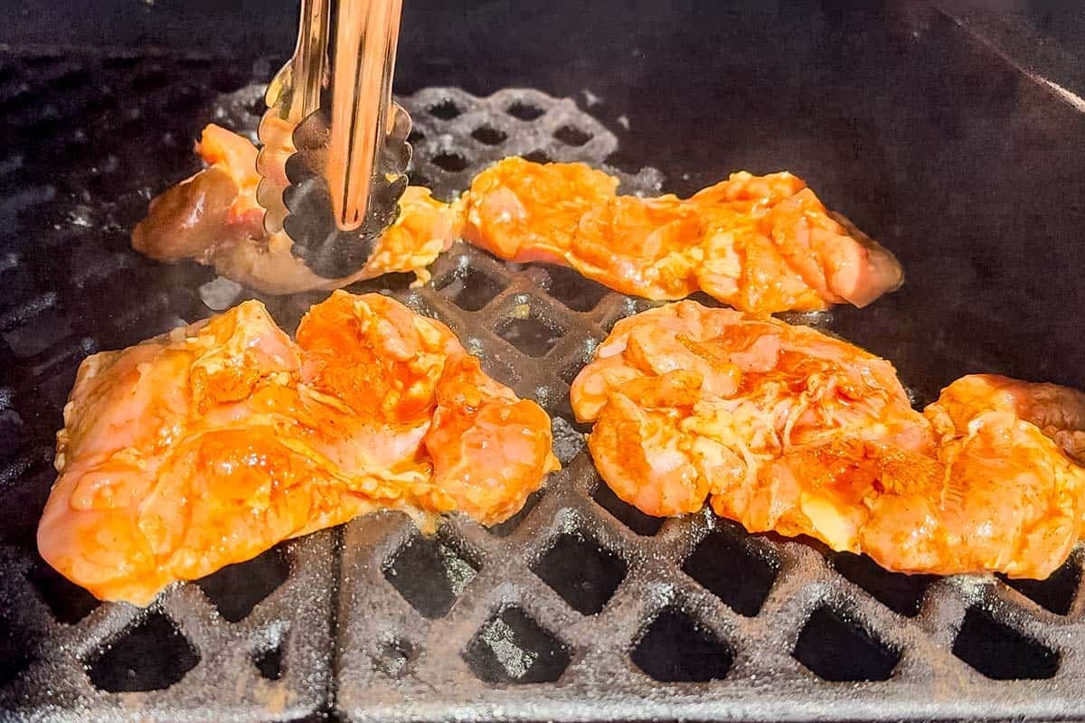 Adding the chicken to a hot grill with metal tongs.