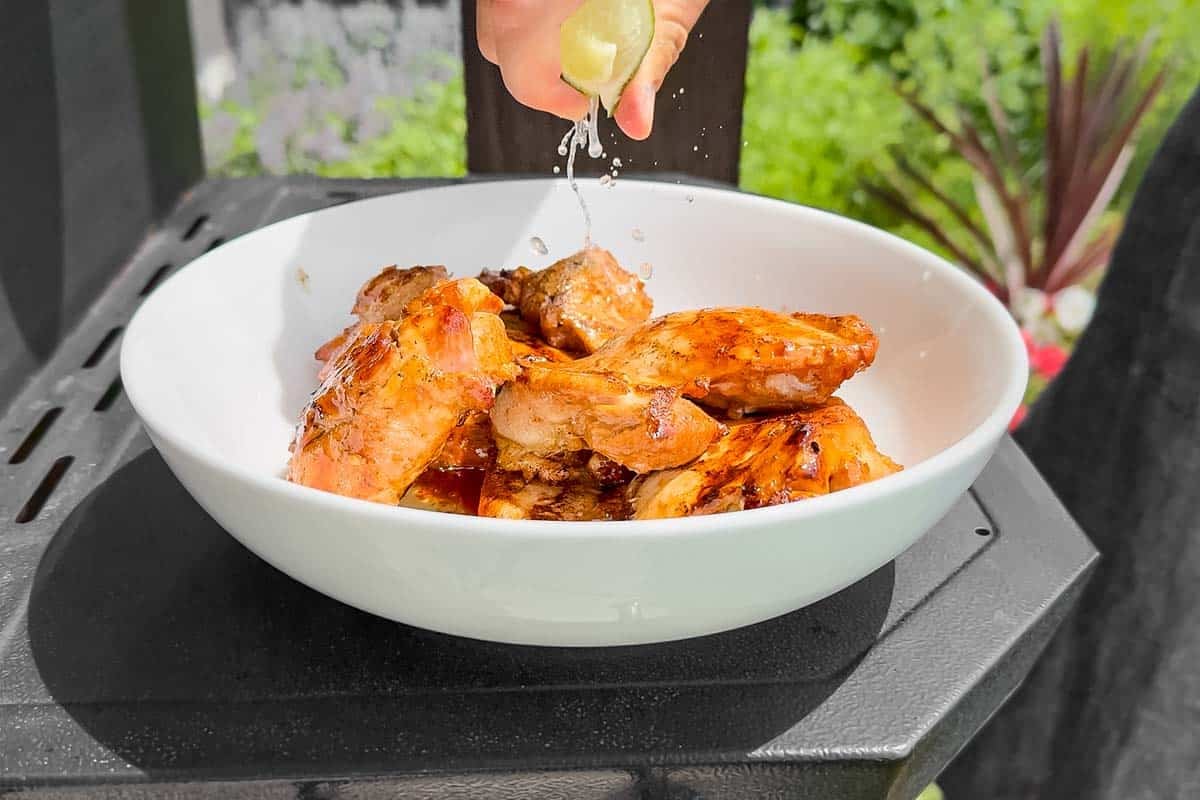 Squeezing lime juice over the grilled chicken in a white bowl.