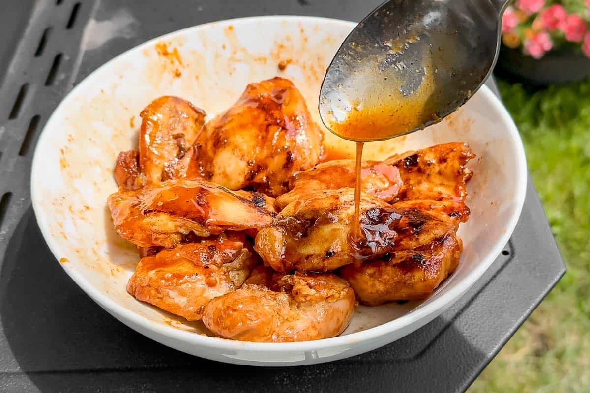 Tossing the grilled chicken thighs with the honey, sriracha, lime mixture in a white bowl.