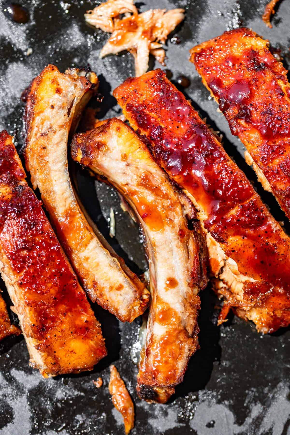 Sliced up bbq ribs on a black cutting board with drips of bbq sauce on them.