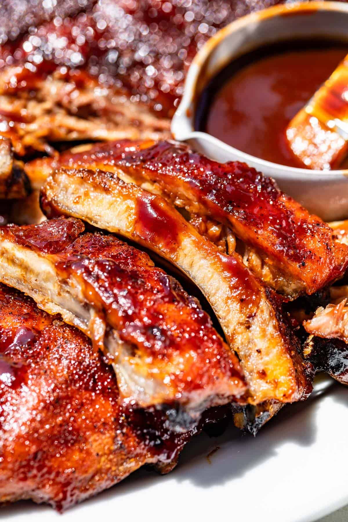 Sliced BBQ ribs with dripping bbq sauce and bowl of bbq sauce on the side.