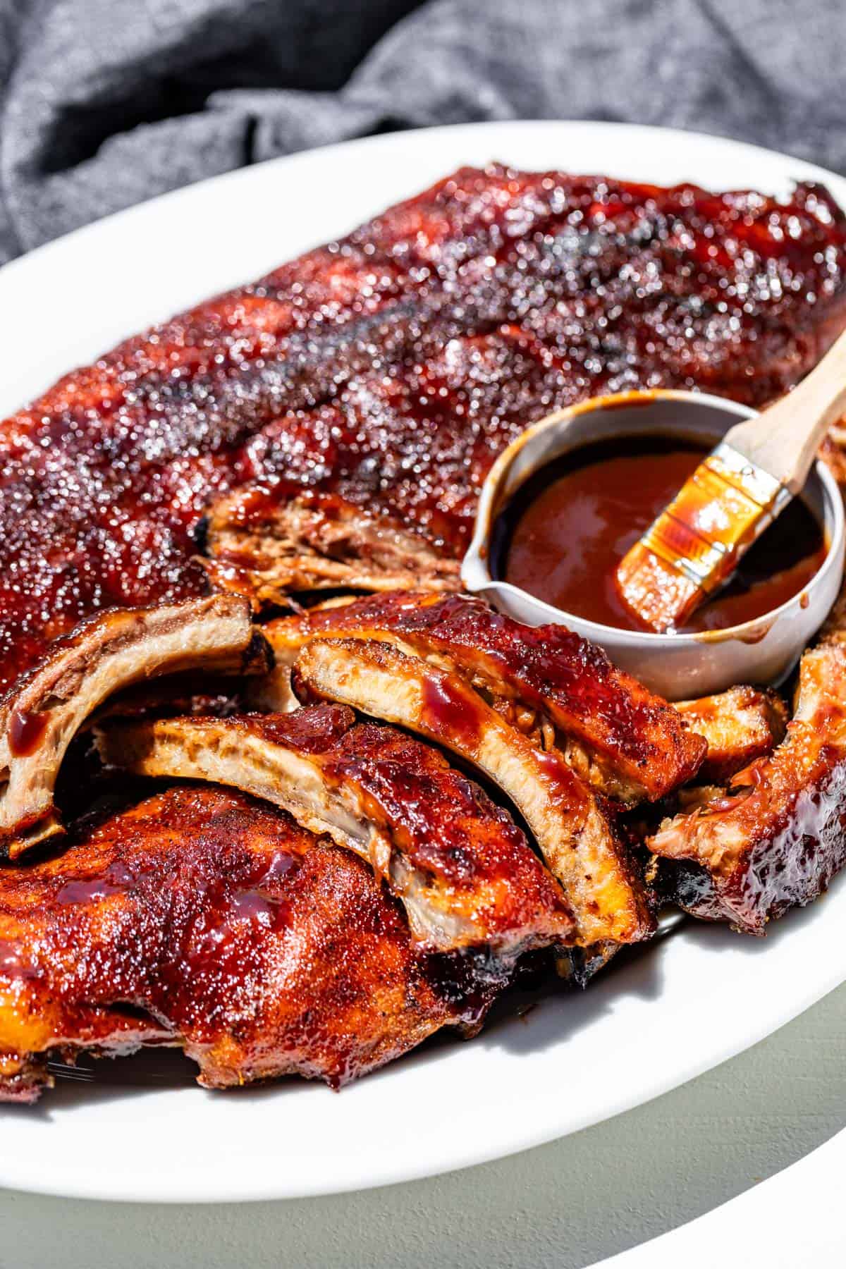 A large white platter with a rack of ribs on one side and sliced bbq ribs on the other.