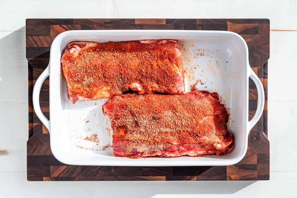 Ribs coated in the spice mixture in a white baking dish.