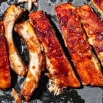 Slicing the ribs on a black wooden cutting board with some bbq sauce on the side.