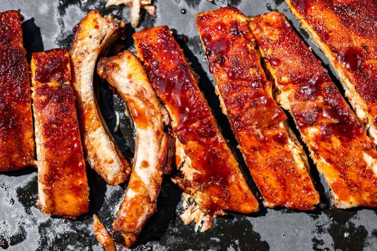 Slicing the ribs on a black wooden cutting board with some bbq sauce on the side.