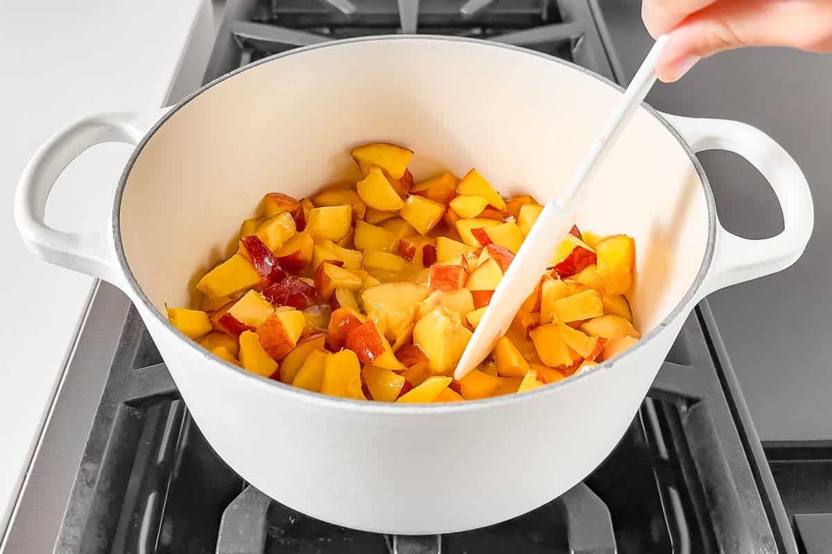 Adding the fresh diced peaches to the maple syrup cornstarch mixture on the stove top.