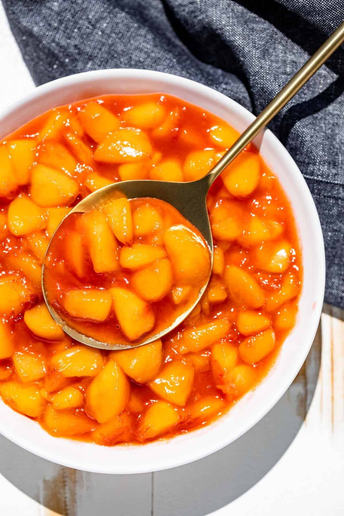Peach Sauce in a large white serving bowl with a gold spoon in it and a blue linen in the background.