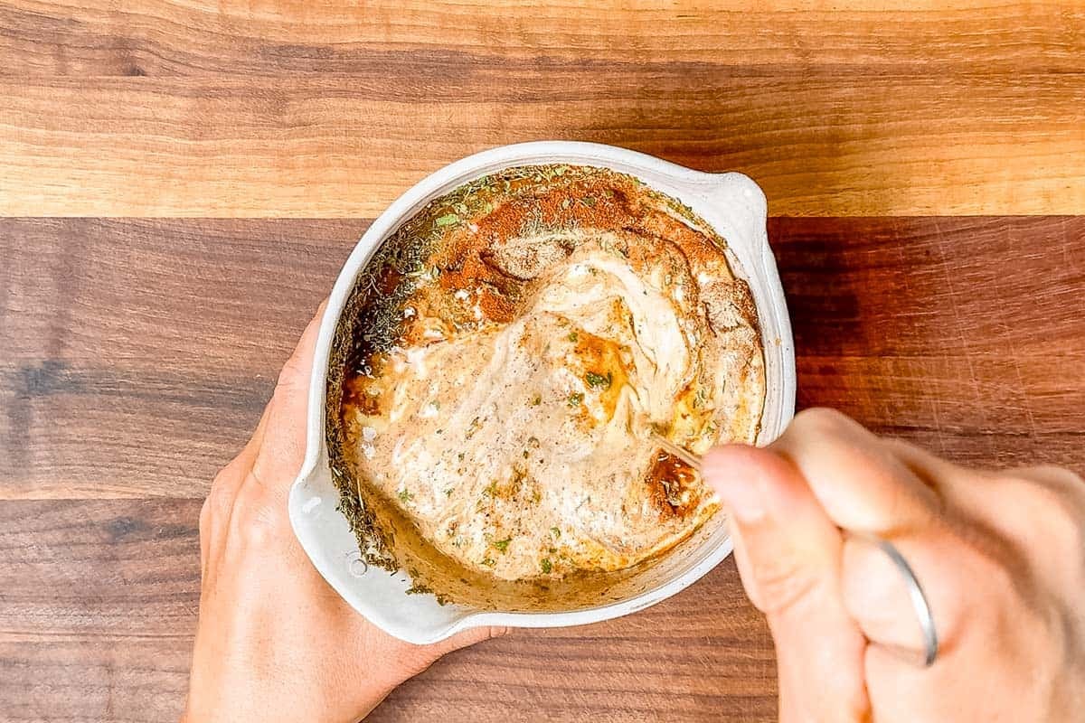 Mixing the chipotle ranch with a metal whisk in a pottery bowl on a wood cutting board.