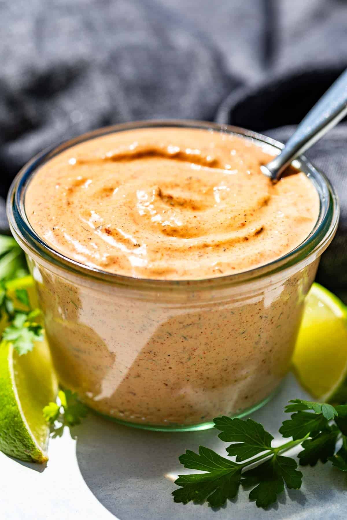 Chipotle Ranch in a clear glass jar with lime wedges and cilantro around it.