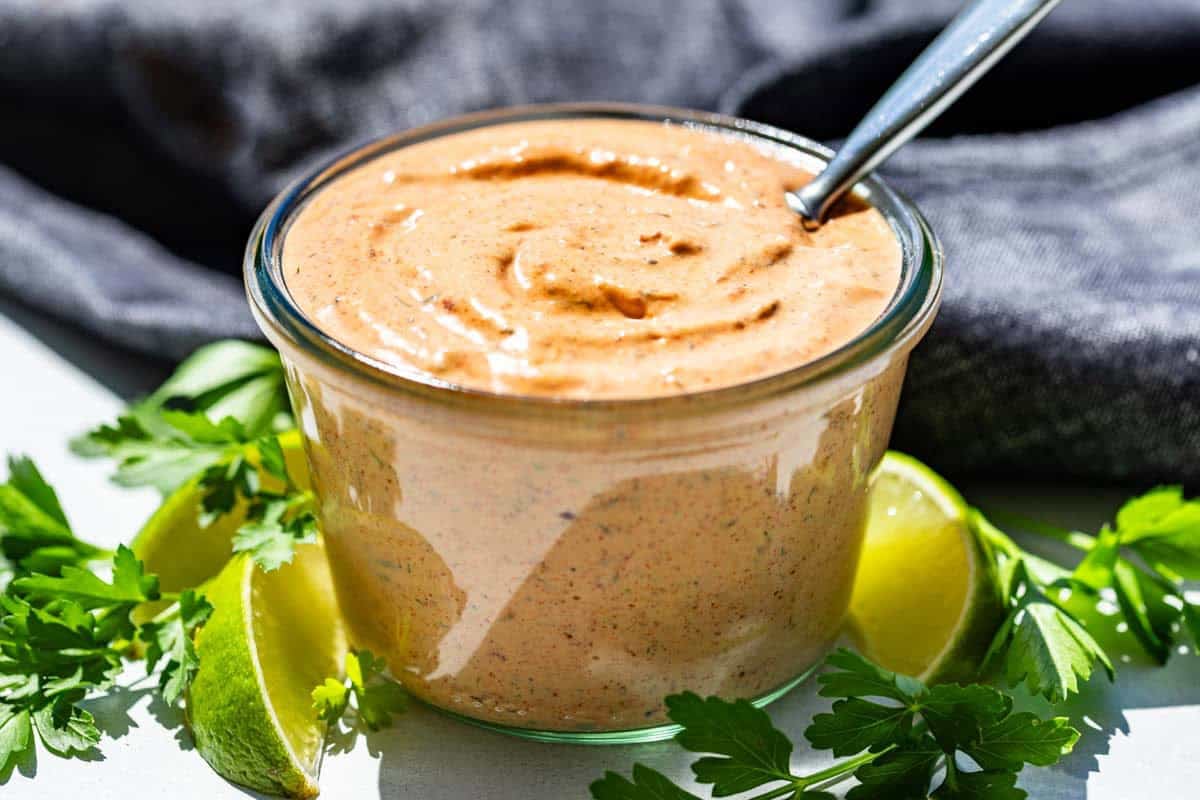 Finished chipotle ranch in a glass container with lime wedges and cilantro sprigs around it.