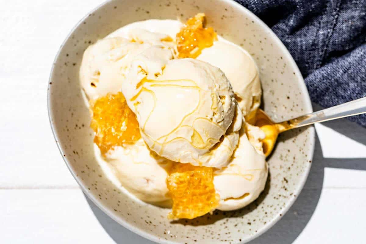Five scoops in a pottery bowl with a gold spoon, drizzled with honey and a blue linen on the side.