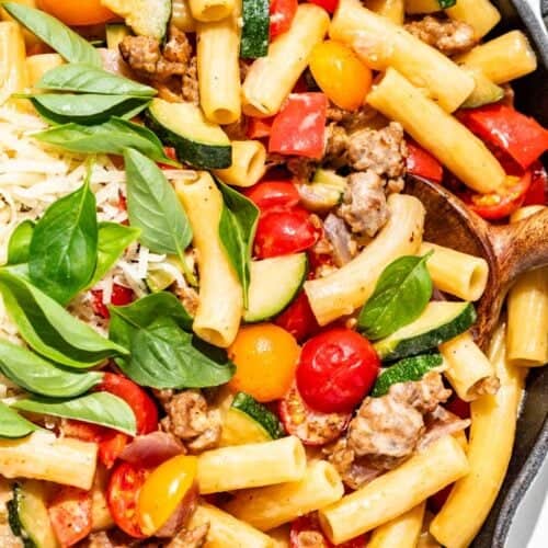 Sausage pepper pasta with zucchini, tomatoes, basil, and grated parmesan with a wood spoon.