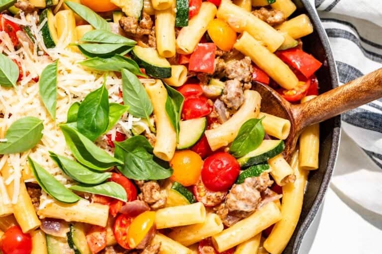 Sausage pepper pasta with zucchini, tomatoes, basil, and grated parmesan with a wood spoon.