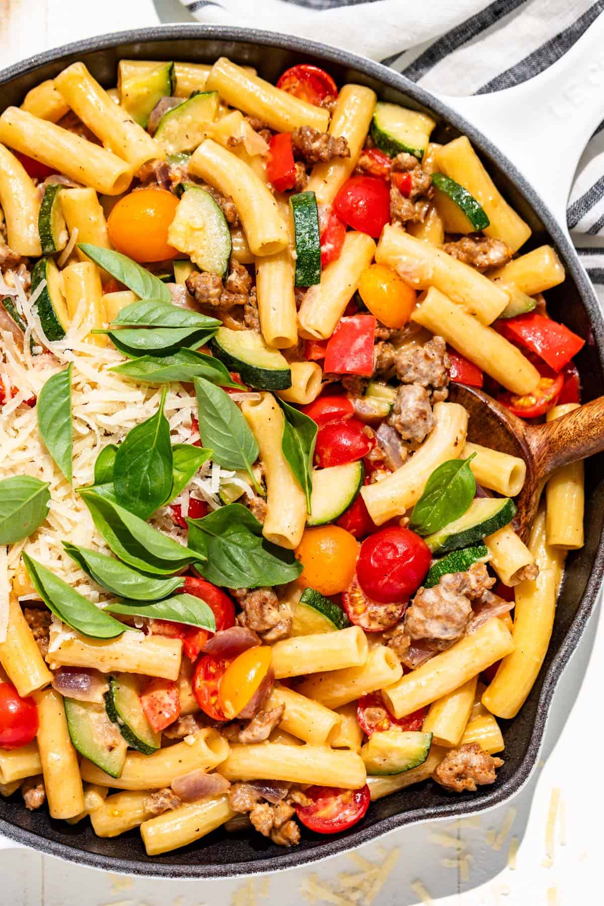 Sausage pepper pasta in a white skillet topped with basil and grated parmesan.