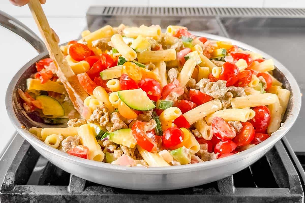 Stirring in the parmesan cheese and cherry tomatoes to the skillet with the sausage and peppers pasta.