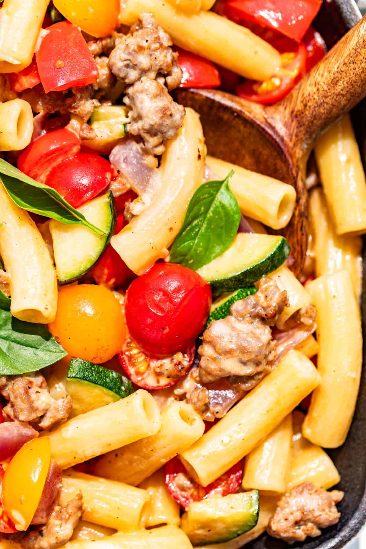 Close view of sausage and peppers pasta on a wood spoon.