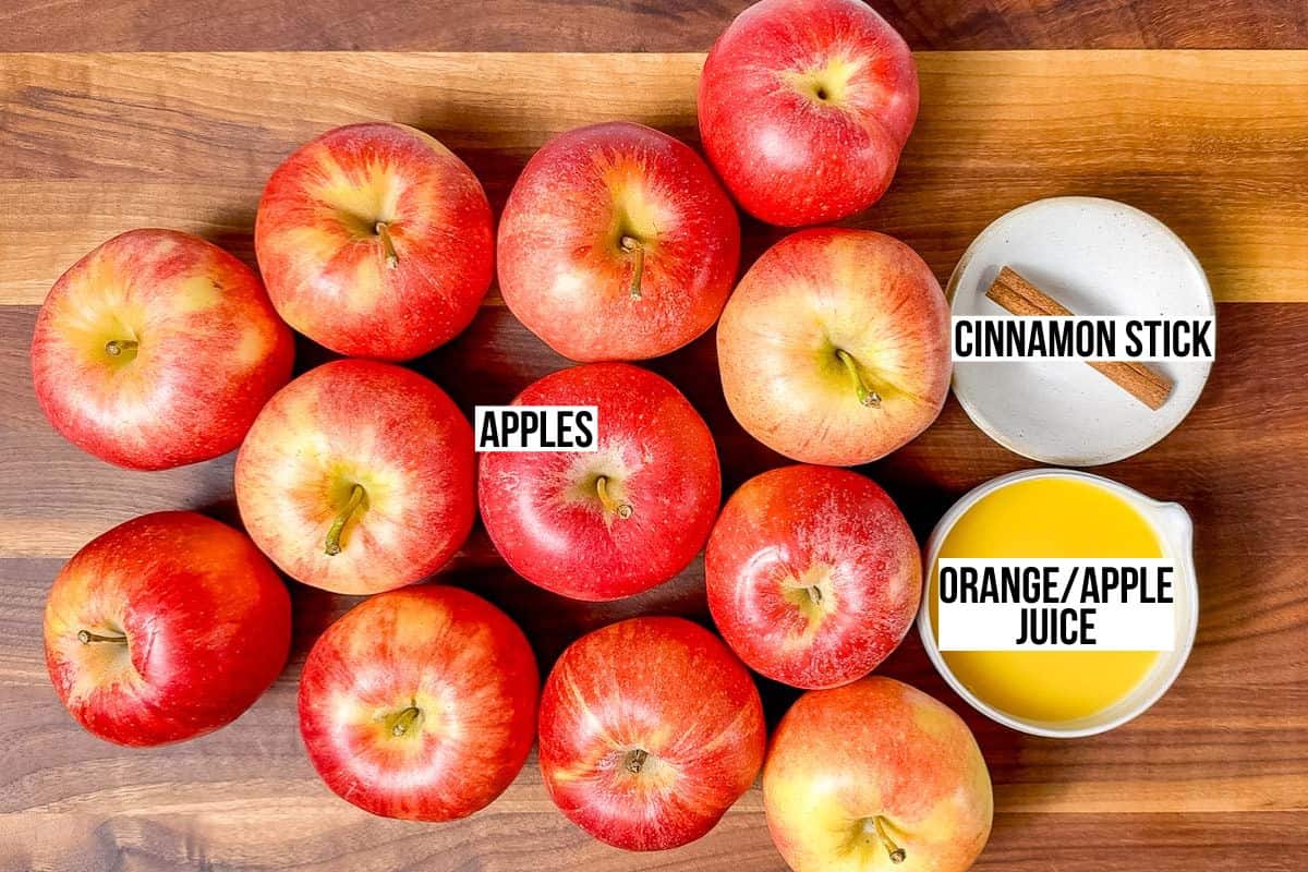 Apples on a cutting board with two bowls of juice and a cinnamon stick.