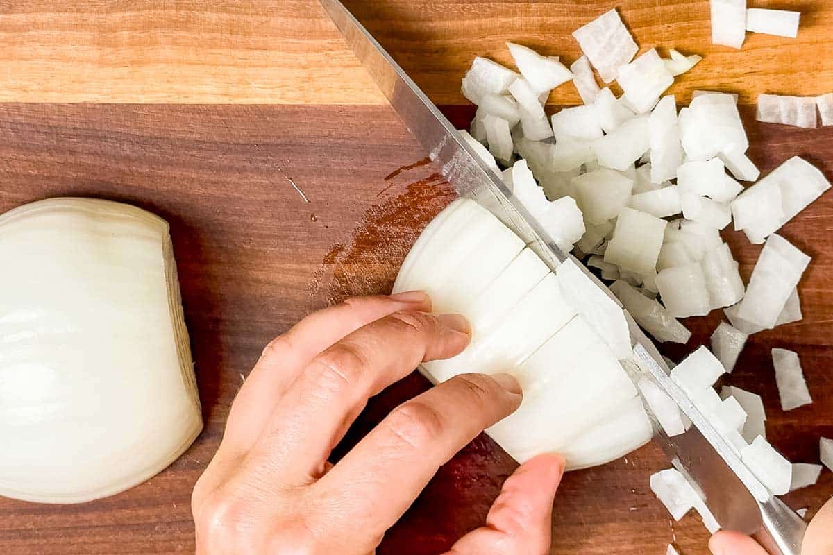 Dicing white onion on a wood cutting board with a chef's knife.