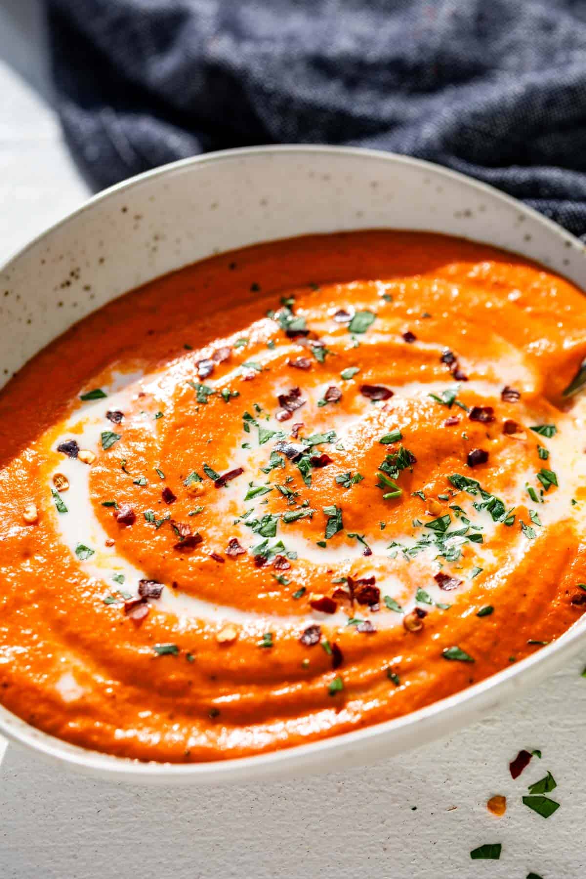 Roasted red pepper sauce in a pottery bowl with a gold spoon and a blue linen in the background.