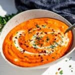 Finished roasted red pepper sauce in a pottery bowl with a gold spoon in it topped with chopped parsley.