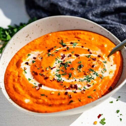 Finished roasted red pepper sauce in a pottery bowl with a gold spoon in it topped with chopped parsley.