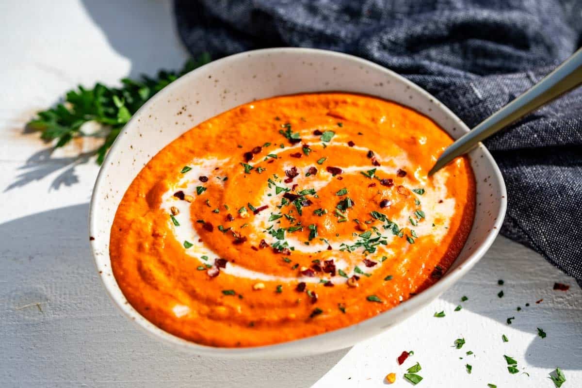 Finished roasted red pepper sauce in a pottery bowl with a gold spoon in it topped with chopped parsley.