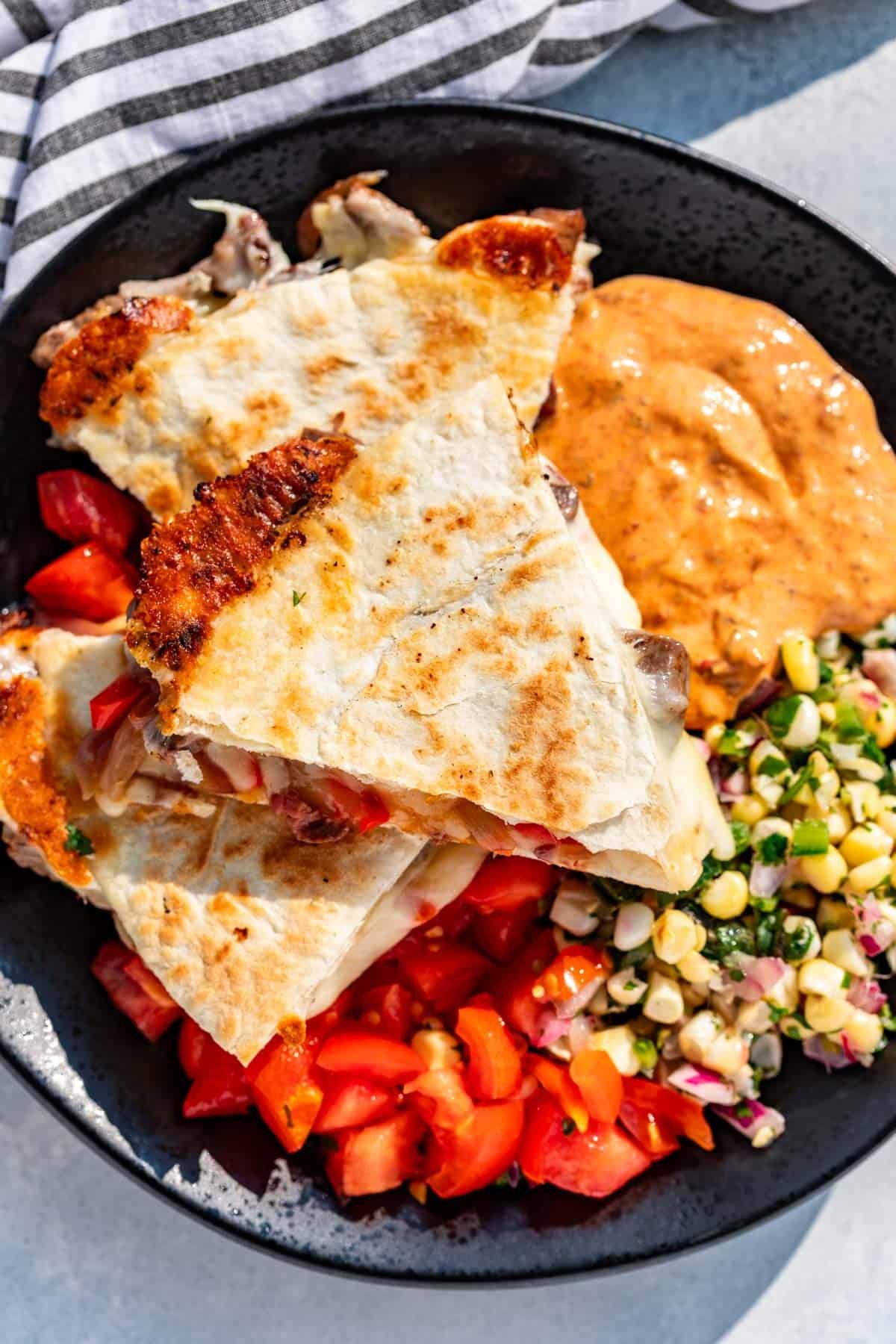 Three wedges of Steak Quesadillas on a plate with Chipotle Ranch, corn salsa, and diced tomatoes.