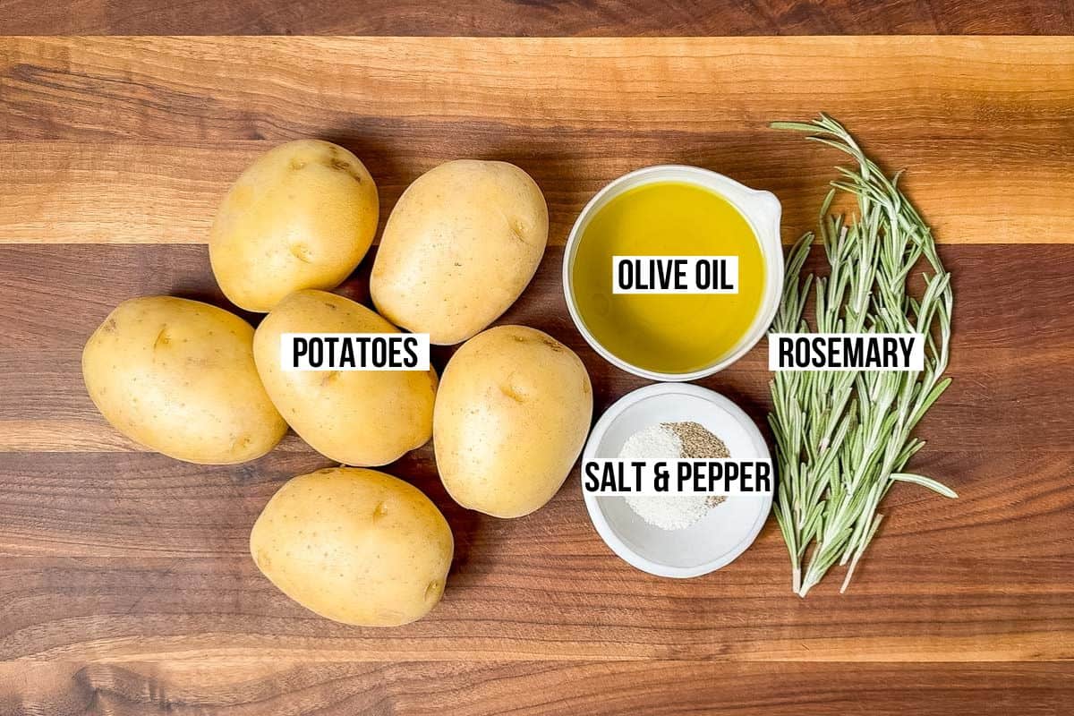 Yukon gold potatoes, olive oil, rosemary, sea salt, and pepper in bowls on a wood cutting board.