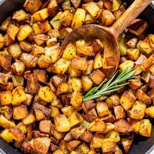 Pan fried potatoes in a white cast iron skillet with a wood spoon scooping some out.